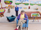 David Hockney seduto su poltrona azzurra nel suo studio d arte circondato da grandi tele prospettiche e paesaggi colorati