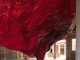 Scultura monumentale in silicone rosso grinzoso appesa al soffitto di un cortile storico veneziano con colonne di pietra