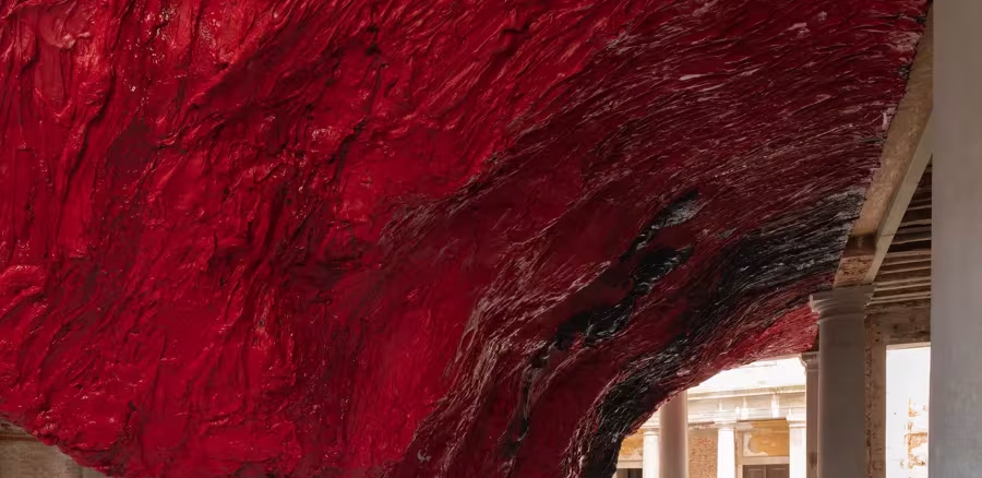 Scultura monumentale in silicone rosso grinzoso appesa al soffitto di un cortile storico veneziano con colonne di pietra