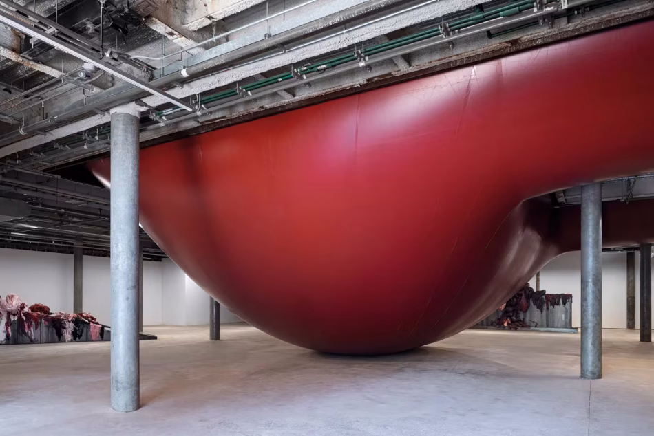 Enorme struttura scultorea flessibile in PVC rosso opaco teso all’interno di una galleria d’arte industriale con colonne