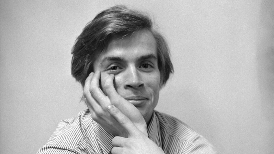 Primo piano in bianco e nero del giovane Rudolf Nureyev con la guancia appoggiata alla mano destra mentre sorride