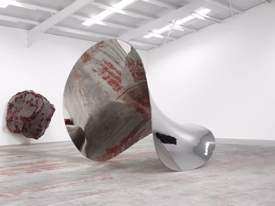 Scultura in acciaio inox lucido ritorta a forma di imbuto specchiante adagiata sul pavimento di una galleria d arte contemporanea