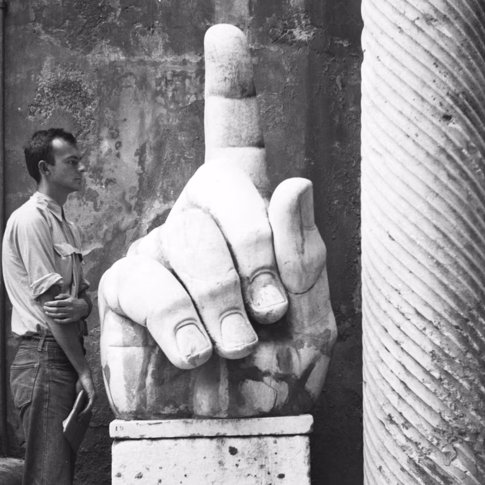 Fotografia storica in bianco e nero di Cy Twombly di profilo accanto a una monumentale mano di marmo romano con il dito indice alzato