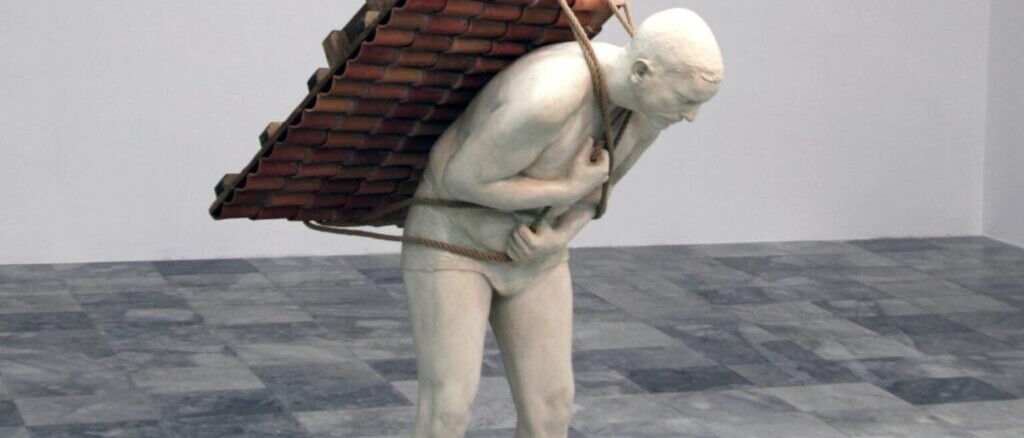 Scultura di un uomo nudo curvato in avanti che trasporta sulla schiena un tetto di tegole legato con corde.
