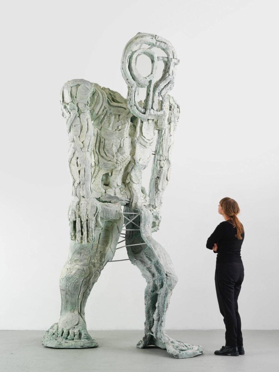 Monumentale scultura antropomorfa stilizzata in gesso bianco e tondini di ferro a vista all'interno di una galleria d'arte.
